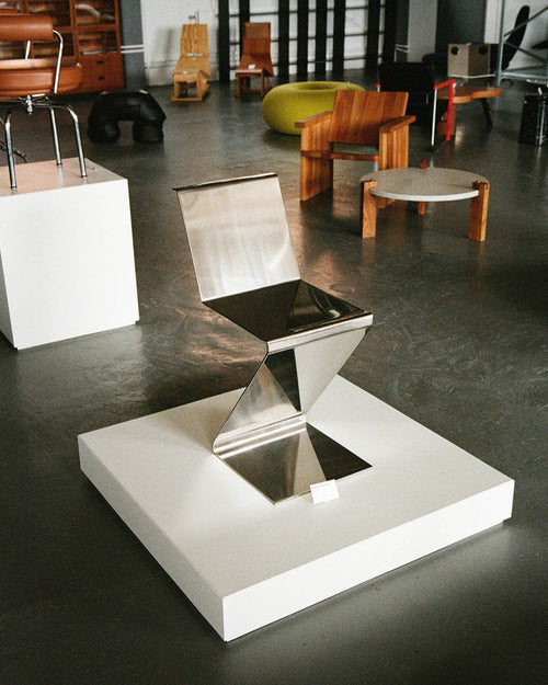Modern chair with reflective surface on a concrete floor in a room with other furniture.