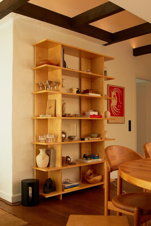 Wooden bookshelf with decorative items in a room with a dining table and chairs.