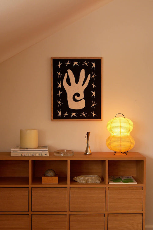 Wooden shelf with a lamp, books, and decorative items against a wall with a framed abstract art piece.