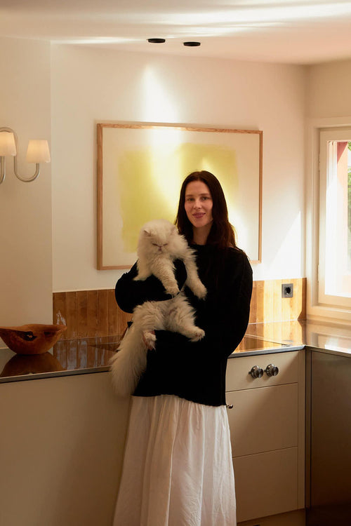Woman holding a cat in a kitchen with a painting on the wall.