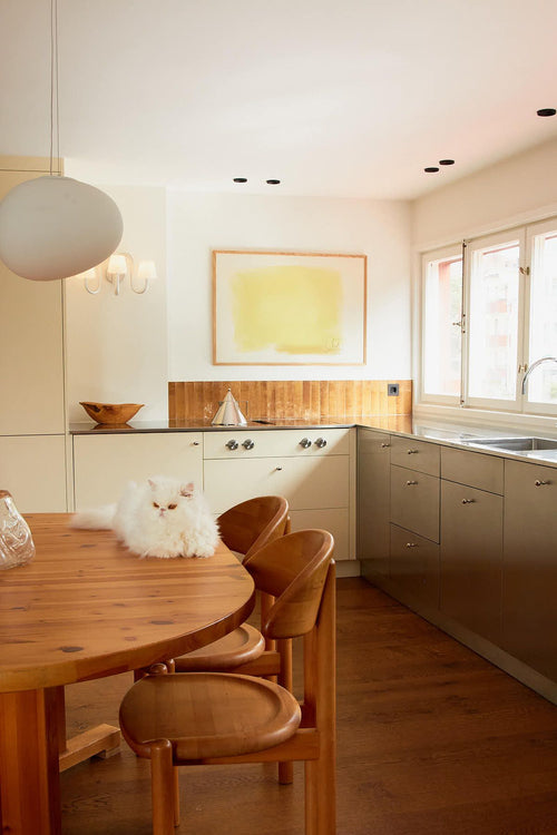 Modern kitchen with wooden dining table and chairs, white cabinets, and a cat on the table.