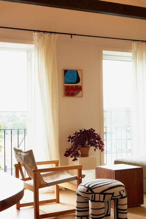 Modern interior with wooden chair, ottoman, and abstract painting on a wall.