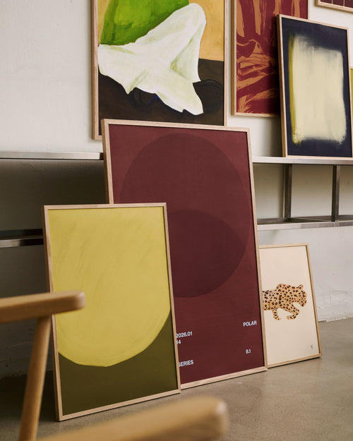 Collection of framed artworks on a wall with a chair in the foreground.