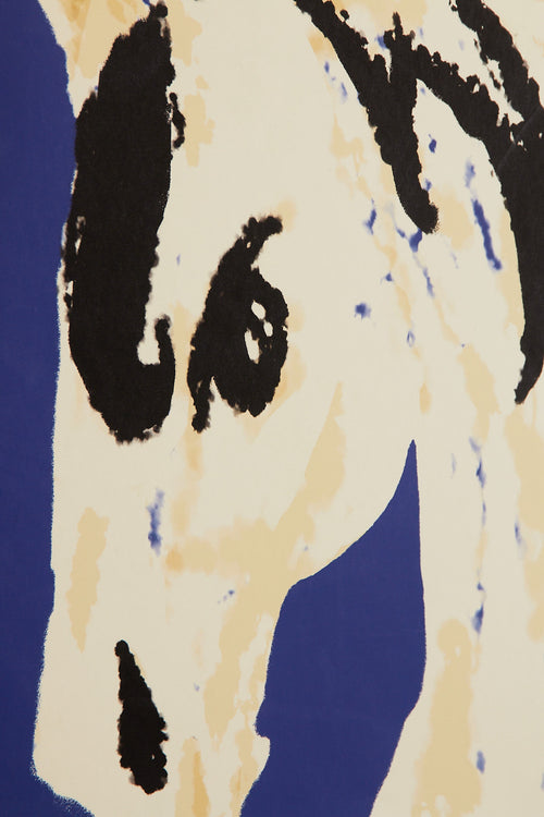 Art print with a stylized illustration of a horse head in light beige and black tones against a cobalt blue background, with an intentionally blurred and painterly feel. Styled in a minimalist interior.