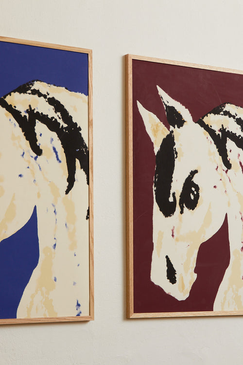 Art print with a stylized illustration of a horse head in light beige and black tones against a wine-red background, with an intentionally blurred and painterly feel. Styled in a minimalist interior.