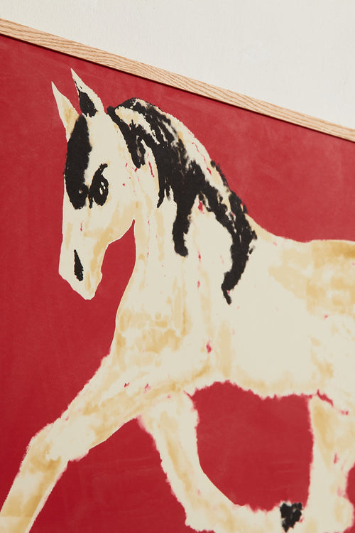 Art print with a stylized illustration of a horse in motion in light beige and black tones against a red background, with an intentionally blurred and painterly feel. Styled in a minimalist interior.