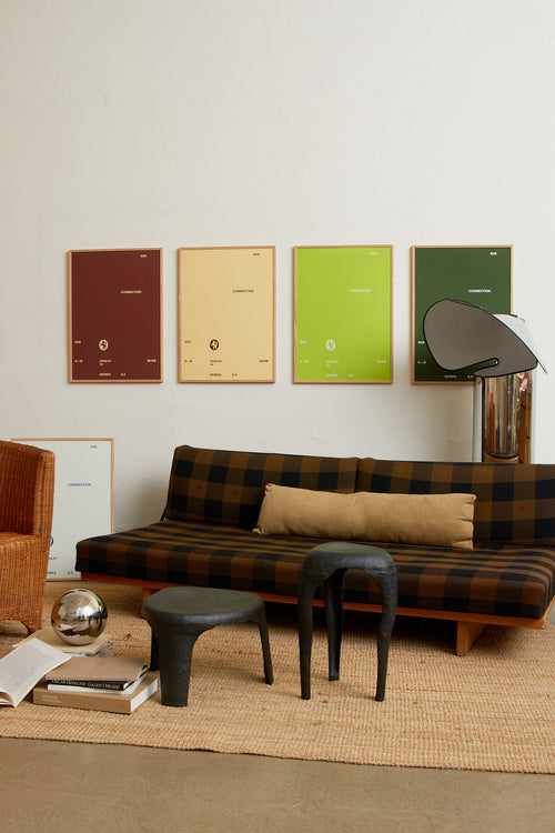 Art print with minimalist, small graphic text elements and a symbol motif in beige against a brown background. Styled in a minimalist interior.