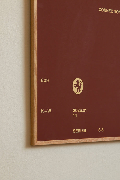 Art print with minimalist, small graphic text elements and a symbol motif in beige against a brown background. Styled in a minimalist interior.