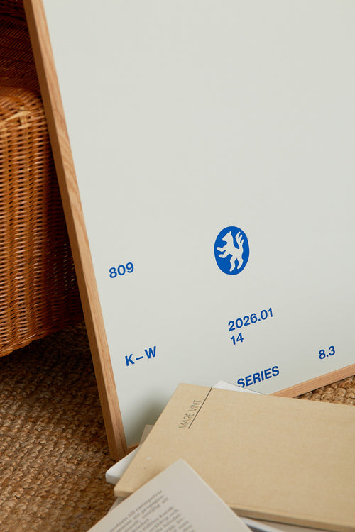 Art print with minimalist, small graphic text elements and a symbol motif in navy blue against a light blue background. Styled in a minimalist interior.