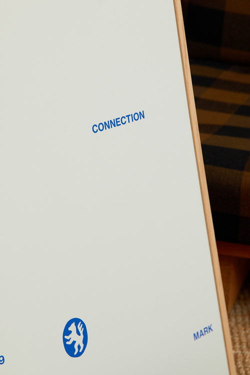 Art print with minimalist, small graphic text elements and a symbol motif in navy blue against a light blue background. Styled in a minimalist interior.