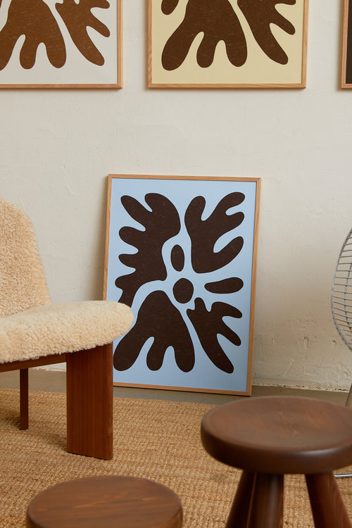 Art print featuring a minimalistic motif in chocolate brown and pastel blue, with shapes that explore the space between abstraction and recognition through soft, fluid forms. Styled in a minimalist interior.