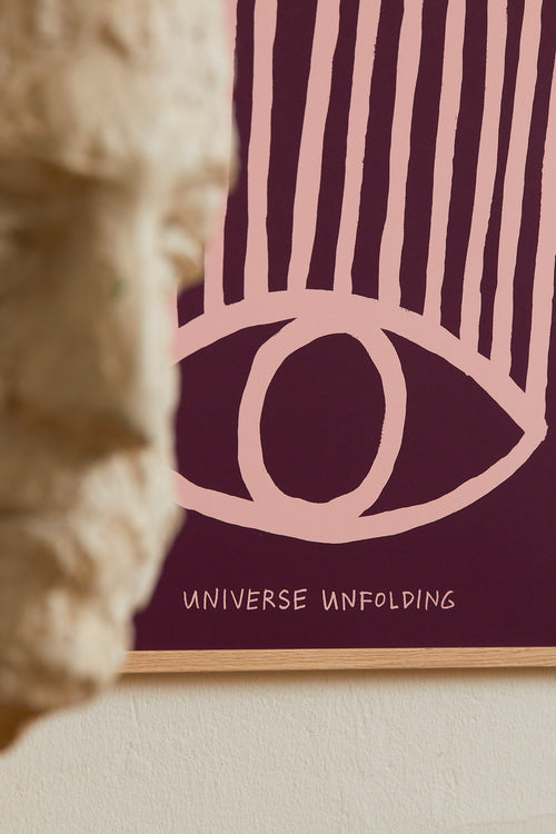 Art print with an abstract colorful, minimalist painting in purple and pink that references an eye. Styled in a minimalist interior.