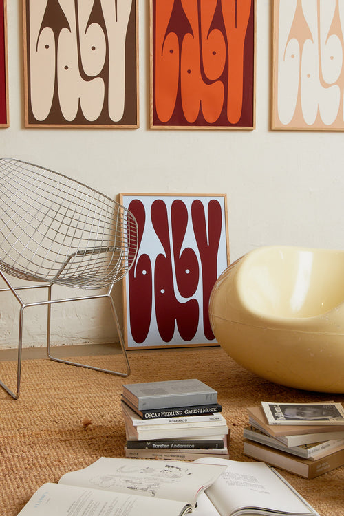 Art print featuring playful, bold typography of the word “Baby” in burgundy against a light blue background. Styled in a minimalist interior.