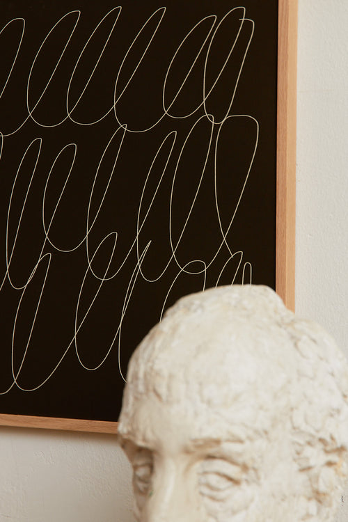 Art print with a graphic illustration of sweeping, continuous lines in a light tone against a dark green background, with a minimalist and abstract expression. Styled in a minimalist interior.