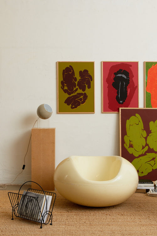 Art print featuring fragmented, rounded forms arranged in loose groupings across a muted green surface, with subtle cracks and glowing edges. Styled in a minimalist interior.