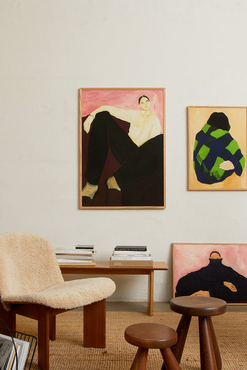Art print featuring a painting of a person resting against a soft burgundy backdrop in front of a pink wall. The outfit is classic yet comfortable, with slippers and a shirt – business at the top, cozy on the feet. Styled in a minimalist interior.