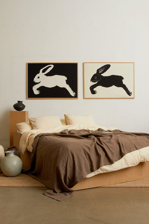 Art print with a stylized illustration of a hare in a dark tone against an off-white background, with a minimalist and graphic expression. Styled in a minimalist interior.