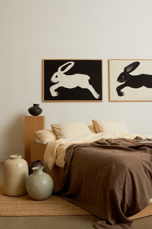 Art print with a stylized illustration of a hare in a light tone against a black background, with a minimalist and graphic expression. Styled in a minimalist interior.