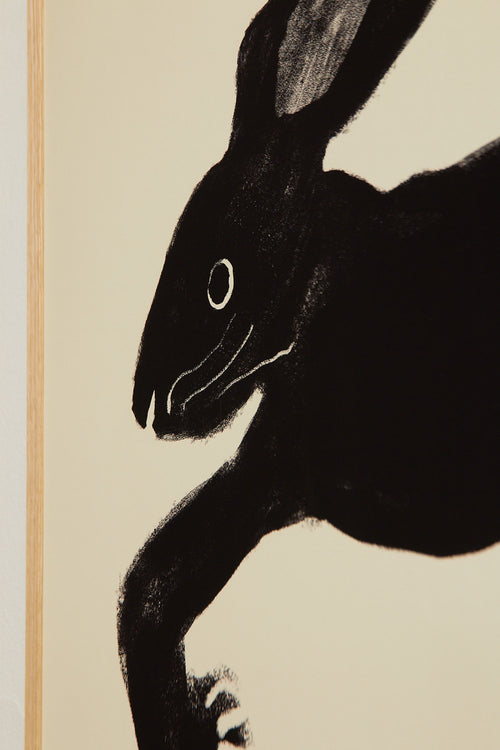 Art print with a stylized illustration of a hare in a dark tone against an off-white background, with a minimalist and graphic expression. Styled in a minimalist interior.