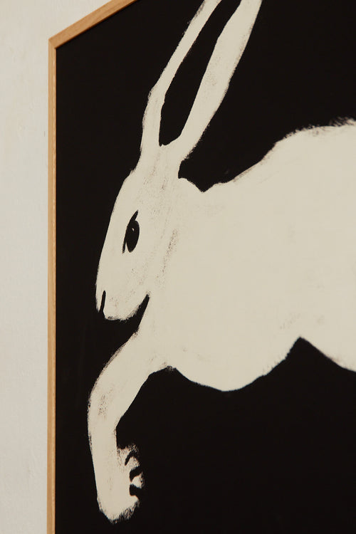 Art print with a stylized illustration of a hare in a light tone against a black background, with a minimalist and graphic expression. Styled in a minimalist interior.