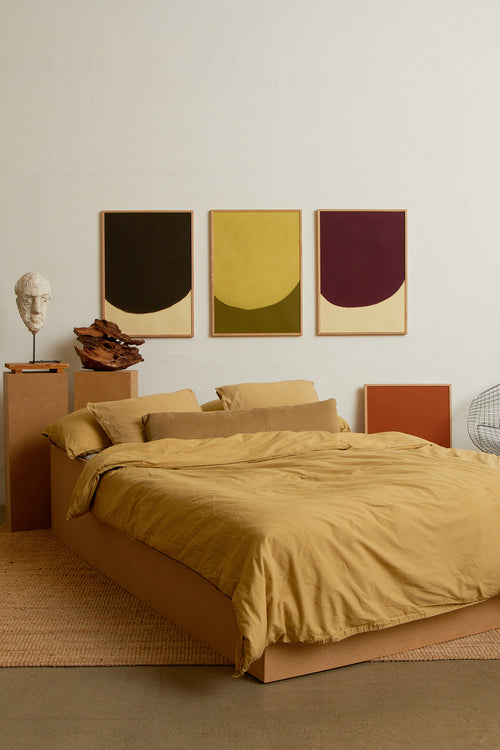 Art print with a minimalist illustration of a large, rounded color field in a yellow tone against a green background. Styled in a minimalist interior.