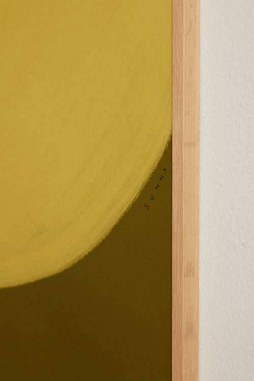 Art print with a minimalist illustration of a large, rounded color field in a yellow tone against a green background. Styled in a minimalist interior.