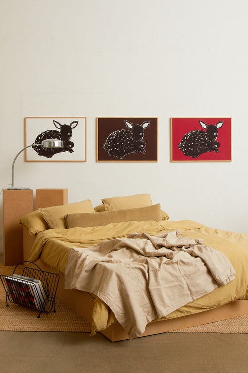 Art print with a stylized illustration of a lying deer in a dark tone against a bright red background, with a minimalist and graphic expression. Styled in a minimalist interior.