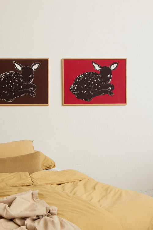 Art print with a stylized illustration of a lying deer in a dark tone against a bright red background, with a minimalist and graphic expression. Styled in a minimalist interior.
