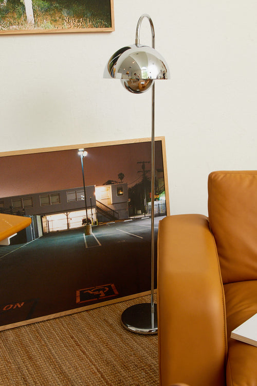 Brown leather sofa with a floor lamp and mirror reflecting a building exterior.