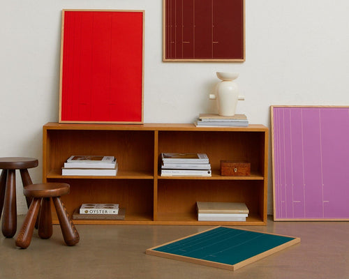 Wooden shelf with books and decor items against a white wall with colorful abstract paintings.