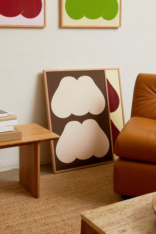 Art print featuring playful, bold typography of the text “MM”, the sound of enjoyment, in off-white against a dark brown background. Styled in a minimalist interior.