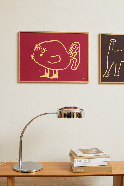 Framed red fish print styled above a desk with a table lamp in a modern interior