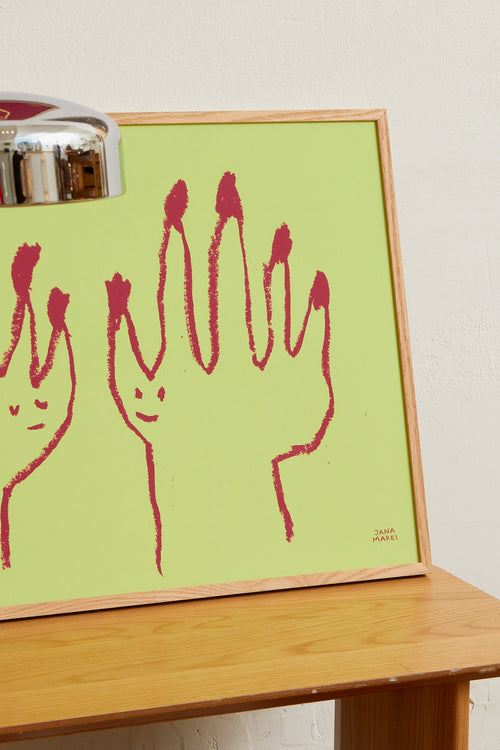 Framed green hands print styled on a wooden shelf in a modern interior