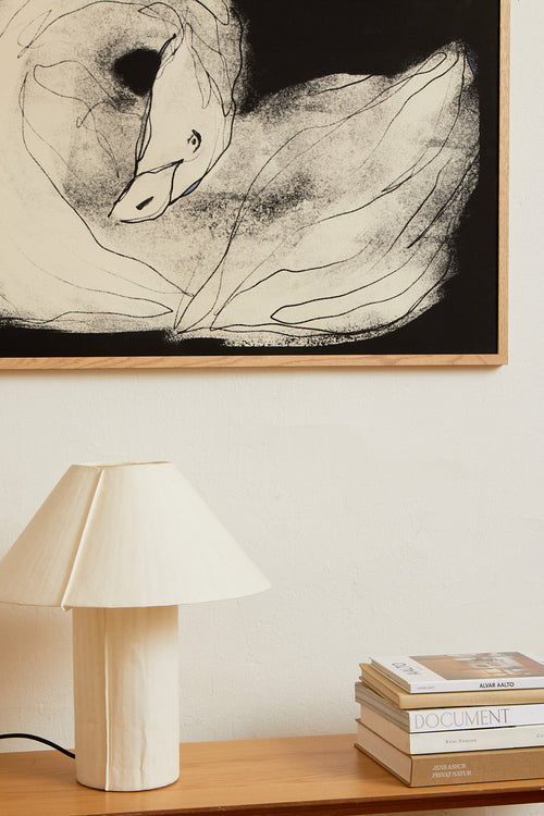 Art print with a stylized illustration of a lying swan in a light tone against a dark background, with a minimalist and graphic expression. Styled in a minimalist interior.