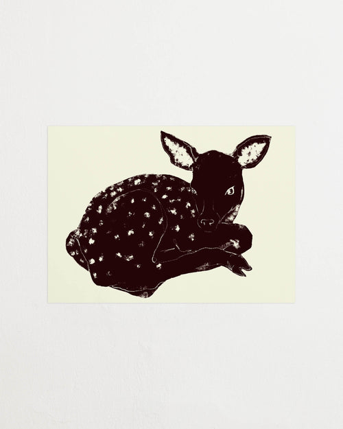 Art print with a stylized illustration of a lying deer in a dark tone against a, with a minimalist and graphic expression. Styled in a minimalist interior.
